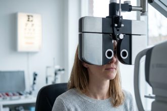 Femme adulte lors d'un contrôle de vue chez l'opticien, regardant à travers un phoroptère dans un cabinet d'optométrie moderne